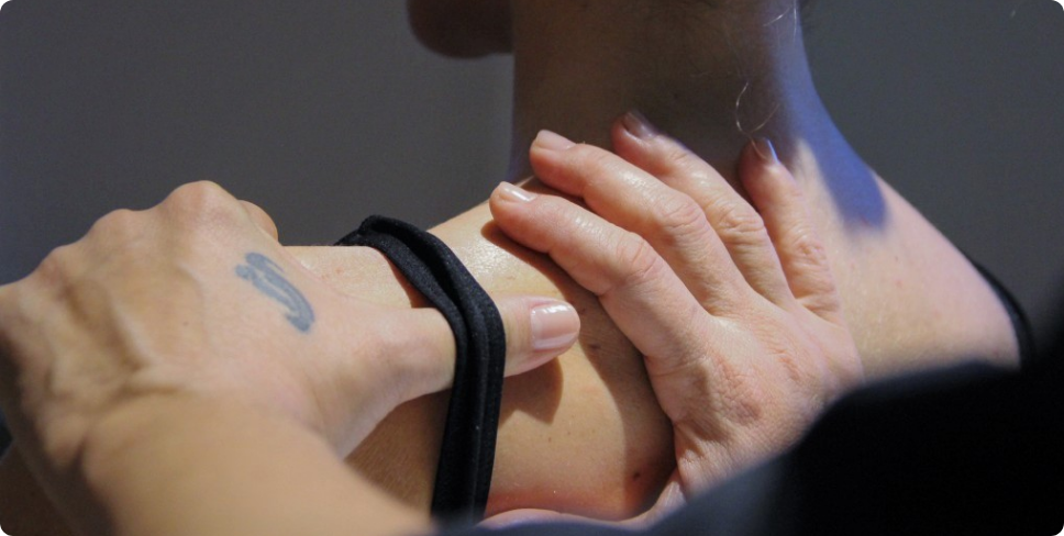 Imagem apresenta uma manobra de RTA, focando nas mãos da Mariângela nas costas de uma paciente. 